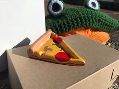 a piece of pizza sitting on top of a cardboard box next to a stuffed frog