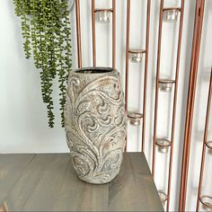 a tall vase sitting on top of a wooden table next to a potted plant