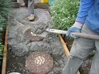 a man with a shovel is working in the ground next to some plants and rocks