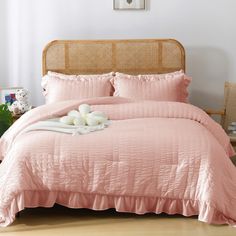 a bed with pink comforter and pillows on top of it in front of a white wall