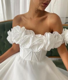 a woman in a white wedding dress sitting on a green chair with her hands behind her back