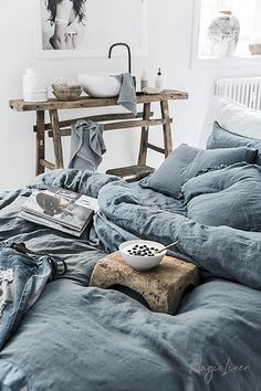 an unmade bed in a white room with blue linens and pillows on it