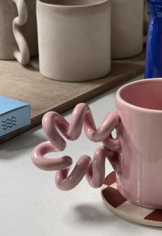 a pink coffee cup sitting on top of a white counter next to a blue book