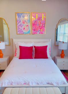 a white bed with pink pillows and two paintings on the wall