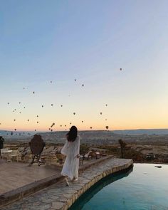 a woman standing next to a pool with hot air balloons in the sky