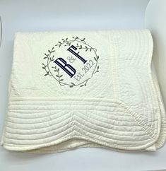 a white quilted blanket with the initials b and f on it, in front of a white background