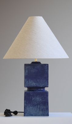 a blue block lamp sitting on top of a table next to a white lampshade