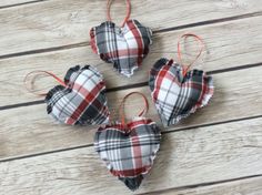 three plaid heart ornaments are hanging on a wooden table