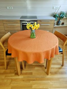 an orange table cloth with yellow flowers in a vase on the top and two wooden chairs around it