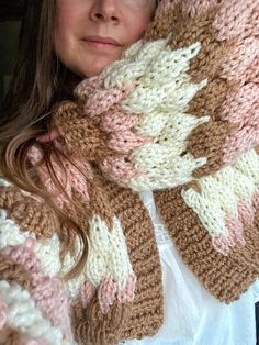 a woman is wearing a knitted scarf in shades of pink, white and brown