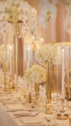 there are many tall gold vases with flowers on the table and candles in them