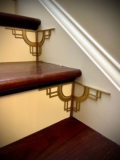 two wooden shelves on the side of a wall next to a white stair case with gold trim