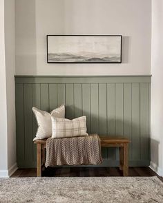 a bench with two pillows on it in front of a green paneled wall and rug