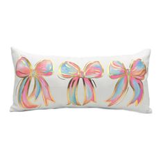 a white pillow with pink bows on the front and blue, green, yellow, and pink ribbons on the back