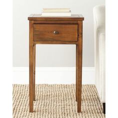 an end table with a book on top and a white chair in the back ground