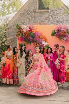 a group of women standing next to each other in front of a wall with flowers