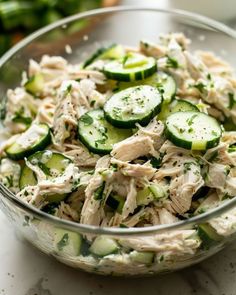 a glass bowl filled with cucumber and chicken salad on top of a table