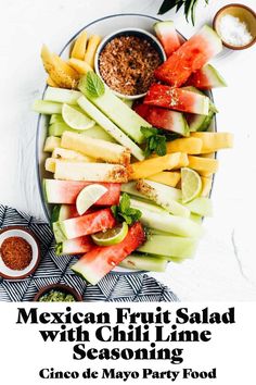 mexican fruit salad with chili lime seasoning on a platter, surrounded by condiments