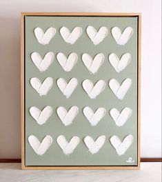 a frame with white hearts cut out of it sitting on a table next to a plant