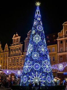 a large christmas tree is lit up in the middle of a town square at night