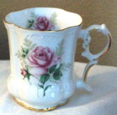 a white and gold coffee cup with pink roses on it's side, next to a pair of scissors