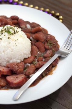 a white plate topped with beans and rice next to a silver fork on top of a wooden table