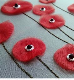 red flowers with black centers are on a table cloth covered in thread and beading