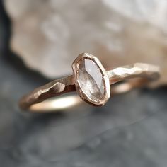 a close up of a gold ring with a white diamond on the top and a rock in the background