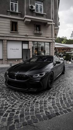 a black car parked in front of a tall building on a cobblestone street