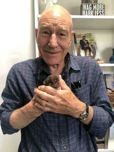 an older man holding a small bird in his hands and looking at the camera with love