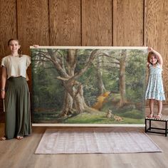 two girls standing next to a painting on the floor in front of a wooden wall