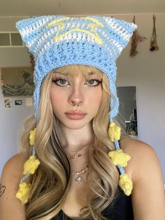 a woman with long blonde hair wearing a crocheted cat hat and yellow tassels