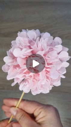 a person holding a pink flower with a stick in it's hand on a wooden surface