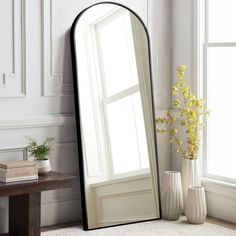 a large mirror sitting on top of a floor next to a vase filled with flowers