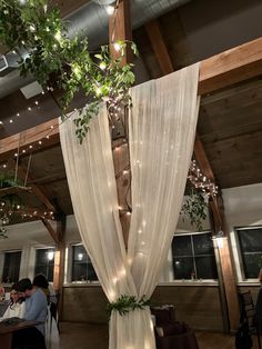 the inside of a restaurant with white curtains and greenery hanging from it's ceiling