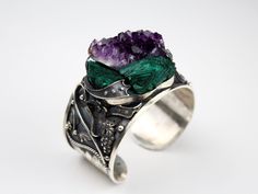 Introducing our exquisite Wide Cuff RAW Malachite Amethyst Sterling Silver Bracelet! This statement piece is a true fusion of natural beauty and contemporary style. Handcrafted with precision, the wide cuff design showcases the mesmerizing combination of raw Malachite and Amethyst gemstones set in gleaming sterling silver. Each stone is meticulously chosen for its unique markings, ensuring a one-of-a-kind piece that exudes luxurious elegance. With its adjustable fit, this bracelet effortlessly transitions from day to night, making it the perfect accessory to elevate any outfit. Embrace the healing properties and stunning allure of this extraordinary bracelet, a must-have for the modern woman with a taste for exceptional craftsmanship. Bracelet weight 89 gr. Wide Cuff Bracelet RAW Malachite Handmade Cuff Jewelry For Anniversary, Handmade Silver Amethyst Cuff Bracelet, Unique Gemstone Cuff Bracelet For Weddings, Unique Wedding Cuff Bracelet With Gemstone, Purple Cuff Bangle Bracelet As Gift, Wearable Art Green Bangle Jewelry, Handmade Amethyst Bangle, Bohemian Amethyst Cuff Bracelet Bangle, Unique Gemstone Cuff Bracelet As A Gift