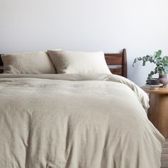 a bed with two pillows on top of it next to a wooden table and potted plant