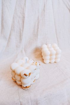 two small candles sitting on top of a white cloth covered table next to each other