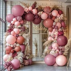 a pink and white balloon arch decorated with flowers, leaves and feathers for a wedding