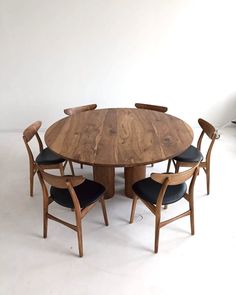 a round wooden table with four chairs around it and a white wall in the background