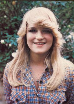 an old photo of a woman with long blonde hair and blue plaid shirt smiling at the camera