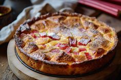 an apple pie with powdered sugar on top is sitting on a wooden table next to a bowl