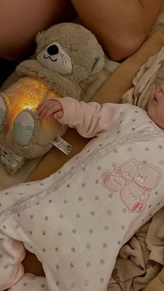 a baby laying on top of a bed next to a teddy bear and a lamp