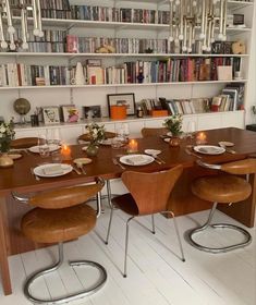 a dining room table with chairs and plates on it in front of bookshelves