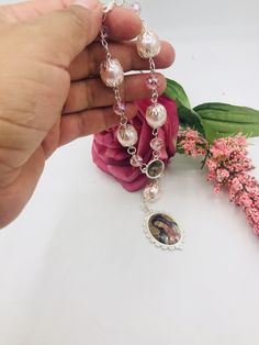 a hand holding a rosary with flowers in the background