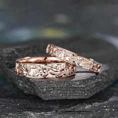 two gold wedding bands sitting on top of a stone slab next to another one with leaves