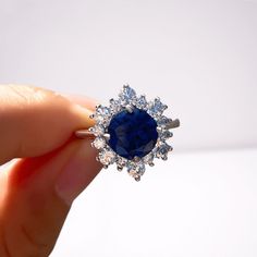 a woman's hand holding an engagement ring with a blue stone surrounded by white diamonds