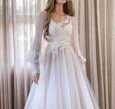 a mannequin wearing a wedding dress with sheer sleeves and flowers on the skirt