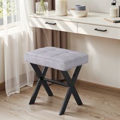 a small stool sitting in front of a window next to a desk with a vase on it