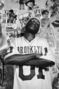 a black and white photo of a man with his arms crossed in front of a wall full of magazines